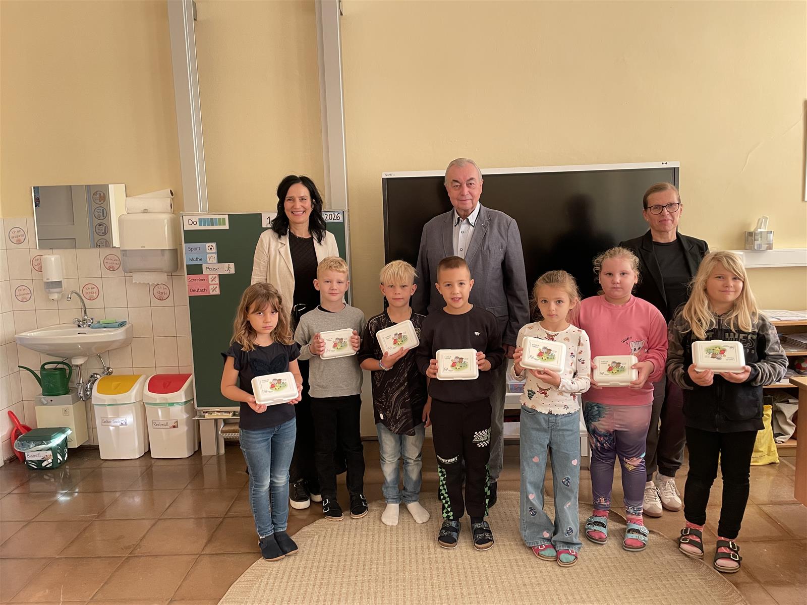 Schüler mit Geschenken in der Schule, zwei Erwachsene stehen hinter ihnen